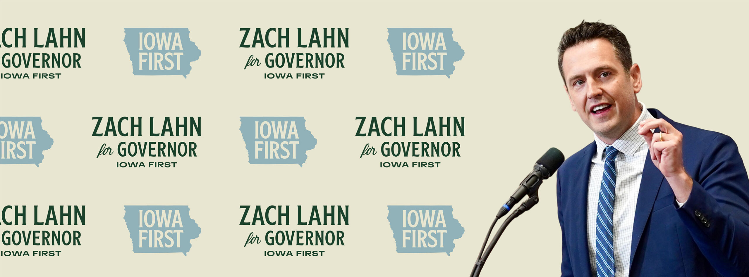 Zach Lahn, candidate for Iowa Governor, speaks into a microphone with a backdrop of repeating